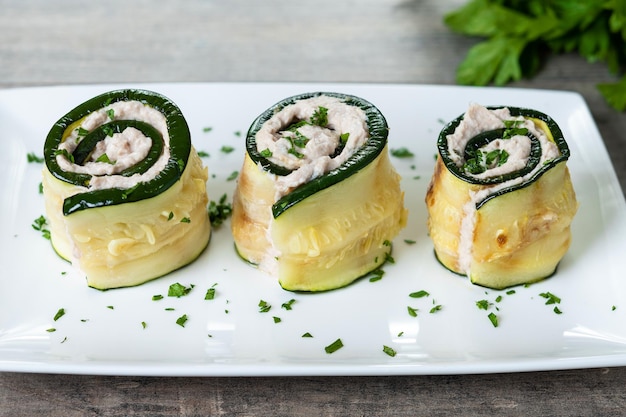 Rouleaux de courgettes grillés farcis de fromage à la crème et de thon sur une table en bois