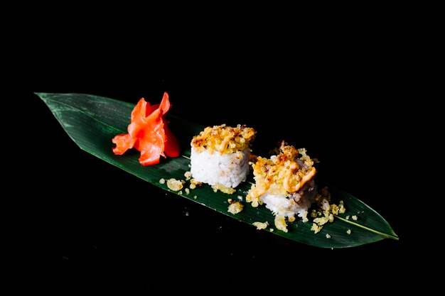 Rouleaux avec des craquelins en haut sur une feuille verte avec du gingembre dans un espace sombre.