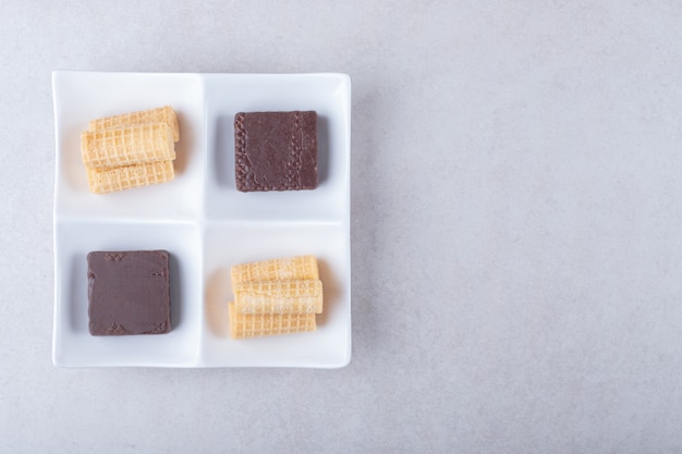 Rouleaux de gaufres et gaufrettes enrobées de chocolat dans un plat sur une table en marbre.