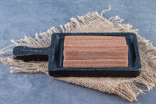 Rouleaux de gaufrettes au chocolat dans une planche sur une texture, sur fond de marbre.