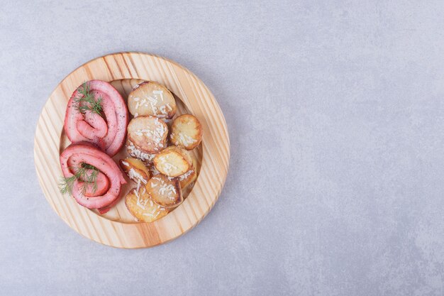 Rouleaux de jambon et pommes de terre frites sur plaque de bois.