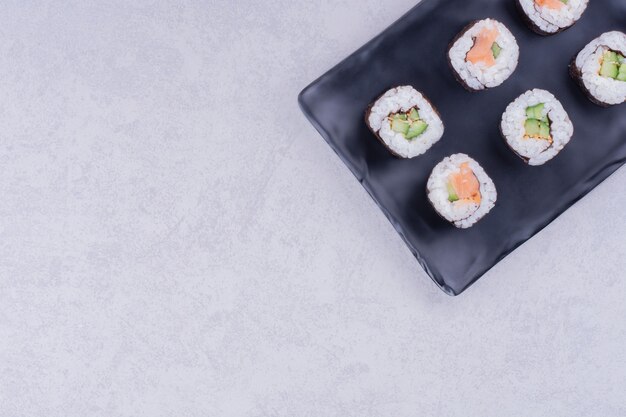 Rouleaux de maki saké dans un plateau en céramique noire