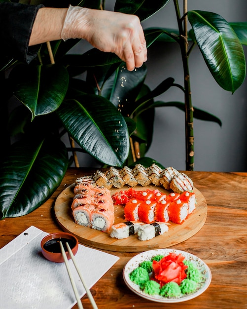 Photo gratuite rouleaux de poisson sur la surface ronde en bois avec des bâtons et de la sauce noire sur la surface grise