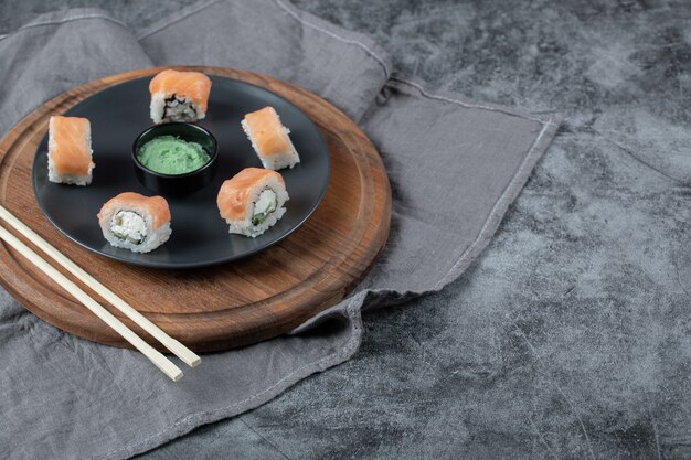 Rouleaux de saumon au fromage à la crème dans une assiette noire avec sauce wasabi.