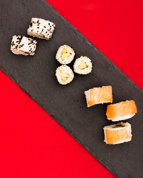 Rouleaux de saumon juteux et sushi sur une plaque de pierre noire sur une surface rouge