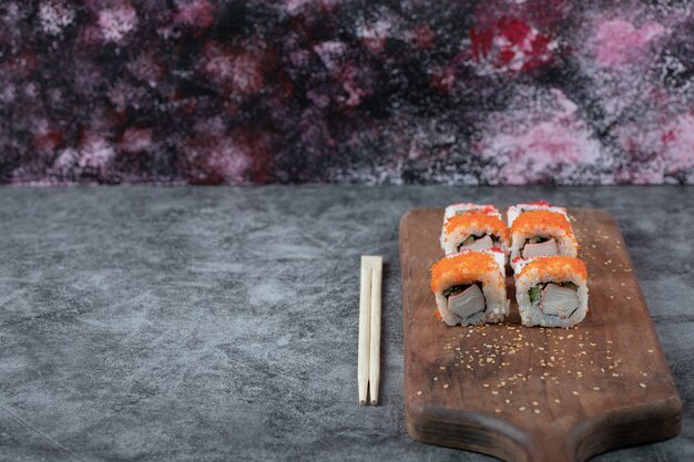 Rouleaux de sushi au caviar jaune et rouge sur une planche de bois.