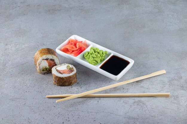 Rouleaux de sushi au thon, wasabi, gingembre et sauce soja sur fond de pierre.