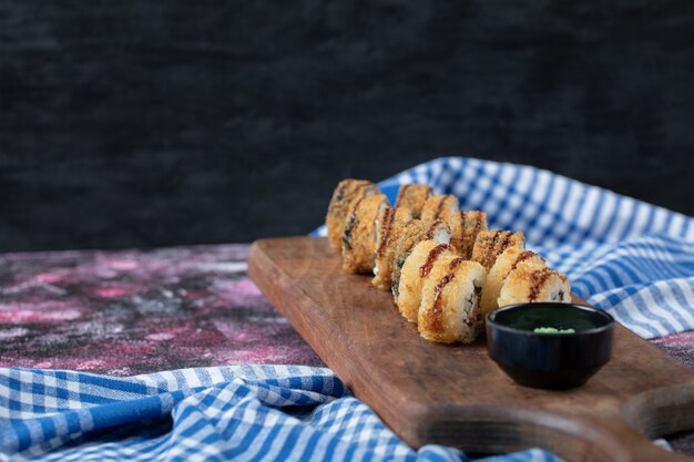 Rouleaux de sushi chauds frits sur une planche de bois avec sauce wasabi.