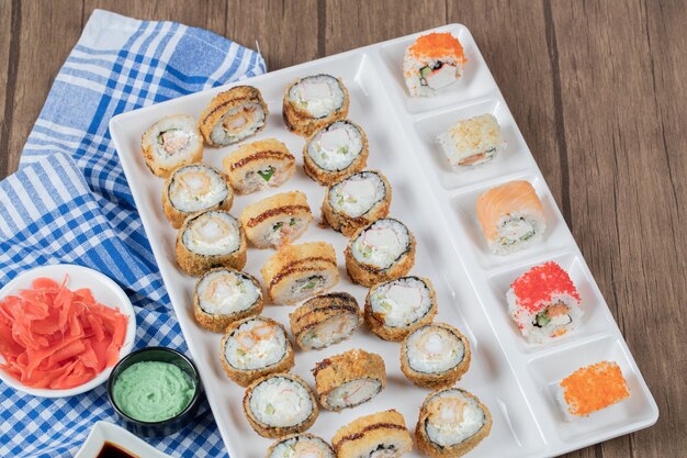 Rouleaux de sushi chauds frits avec sauce soja, wasabi et gingembre sur une serviette à carreaux bleus.