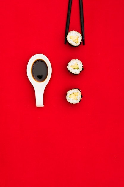 Photo gratuite rouleaux de sushi frais; sauce soja à la cuillère et baguettes noires sur la surface rouge foncé
