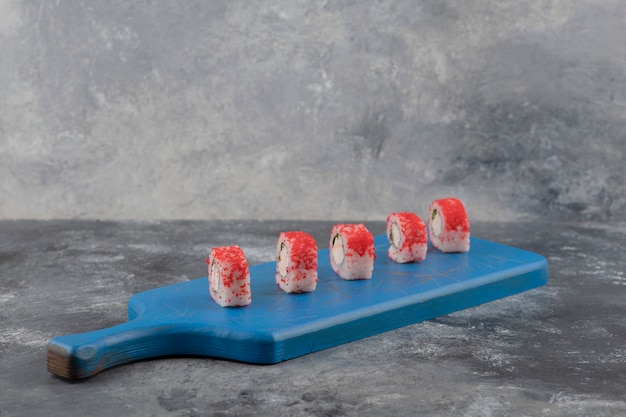 Rouleaux de sushi savoureux avec du caviar rouge sur une planche à découper bleue