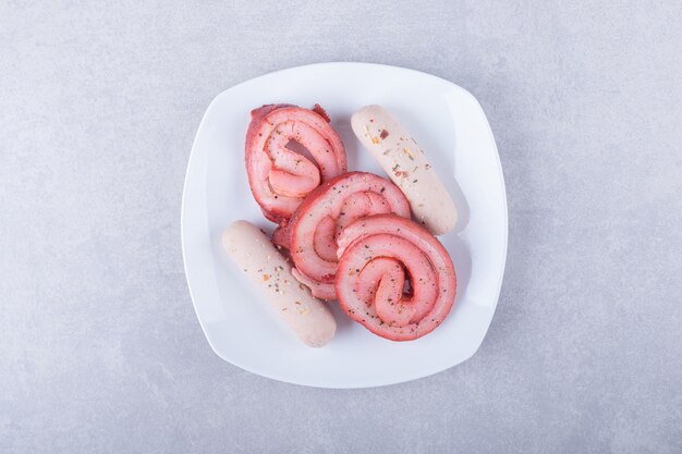 Rouleaux de viande fumée et saucisses sur plaque blanche.