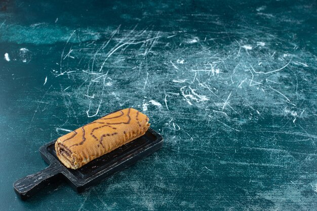 Rouler le gâteau sur une planche, sur la table bleue.