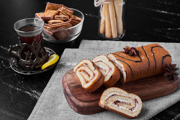 Rouler le gâteau tranché sur une planche de bois et servi avec un verre de thé.