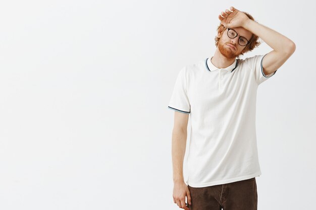 Rousse barbu fatigué posant contre le mur blanc avec des lunettes