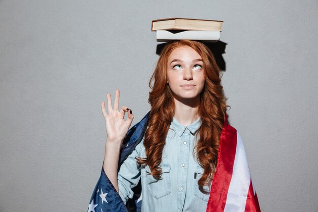 Rousse drôle jeune femme tenant un livre sur la tête portant le drapeau américain