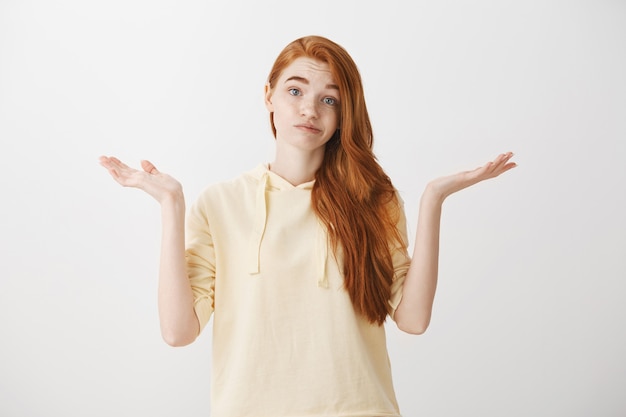 Rousse indécise haussant les épaules avec les mains écartées sur le côté, je ne sais rien