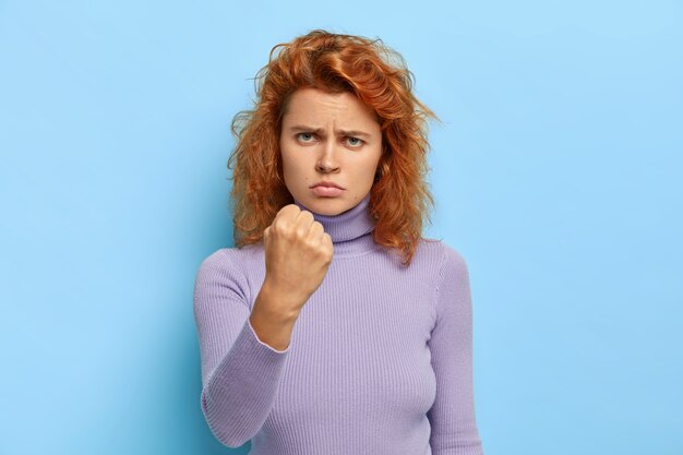 Une rousse sérieuse mécontente et féroce montre le poing serré de colère, prête à relever tous les défis