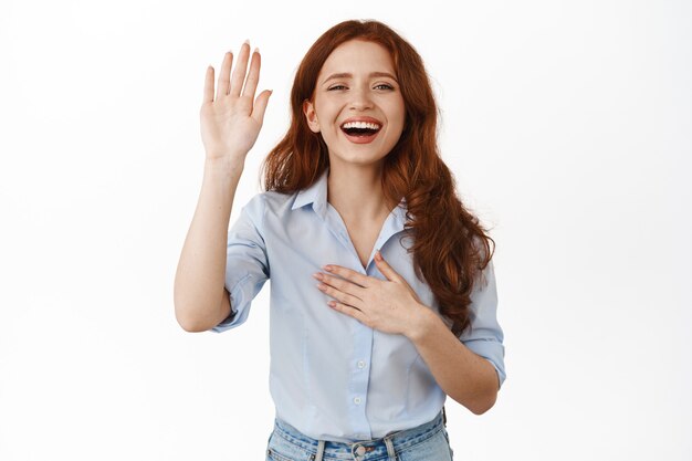 Rousse souriante avec une main levée sur blanc