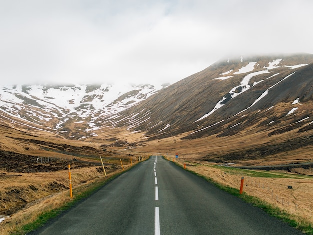 Route entourée de collines couvertes de verdure, de neige et de brouillard en Islande