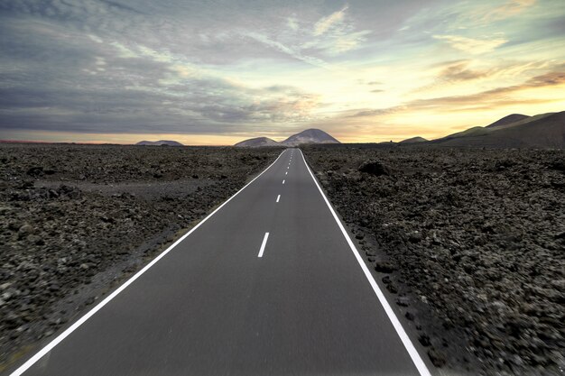 Route entourée de collines et de pierres pendant le coucher du soleil dans le parc national de Timanfaya en Espagne