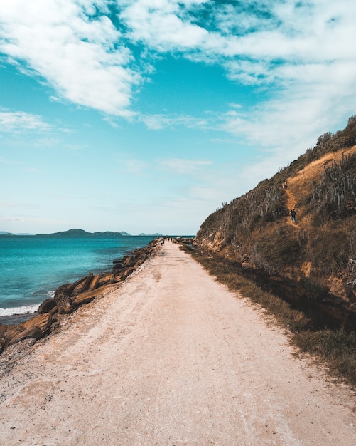 Route de sable étroite longeant la mer et de hautes collines escarpées avec un beau ciel bleu nuageux