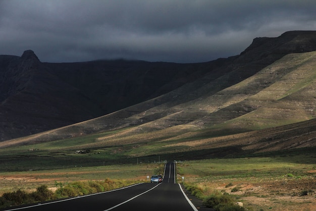 Route avec des voitures roulant au loin au milieu des champs herbeux et des montagnes en arrière-plan