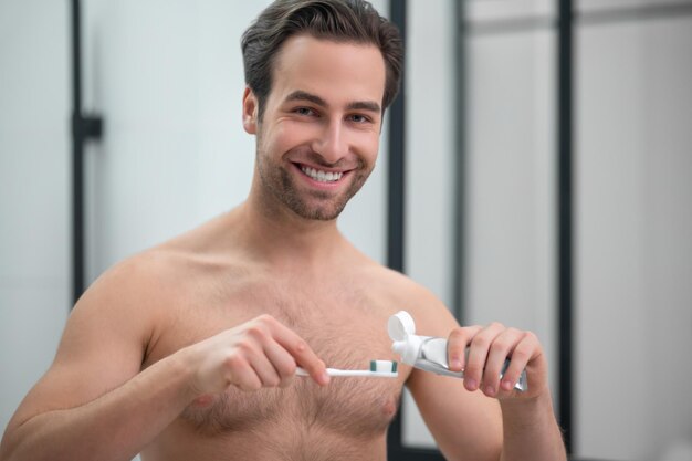 Routine matinale. Jeune bel homme serrant le dentifrice sur une brosse à dents