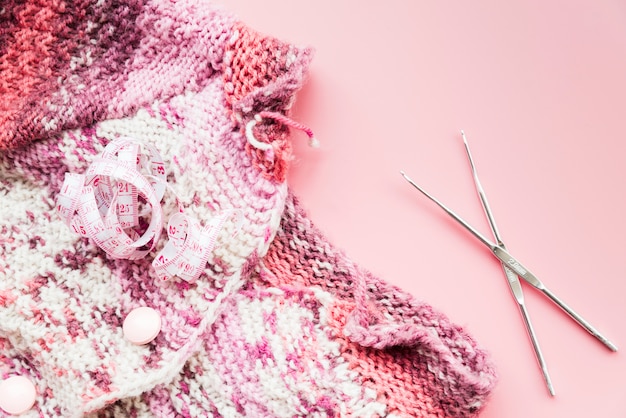 Ruban à mesurer avec crochet à tricoter et aiguilles sur fond rose