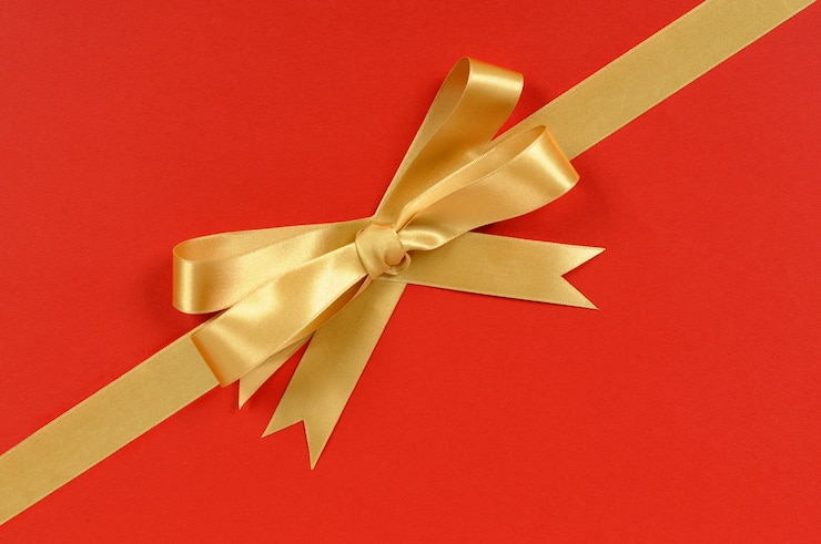 Photo gratuit ruban d'or bow cadeau coin diagonale isolé sur fond de papier d'emballage rouge