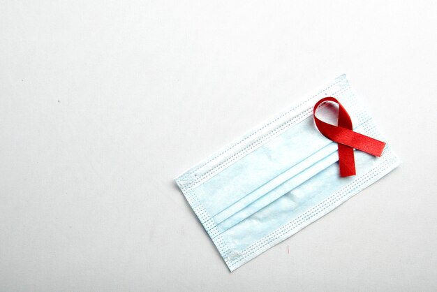 Ruban rouge et masque facial avec fond blanc. Sensibilisation au ruban VIH sida