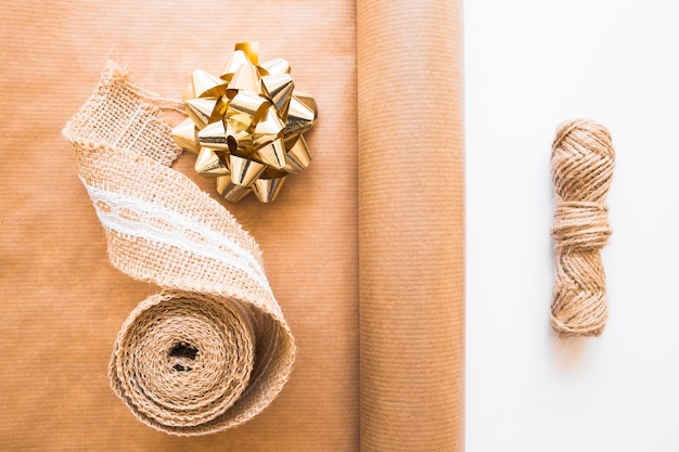 Photo gratuite ruban de tissage; arc d'or; papier cadeau marron et chaîne de jute sur fond blanc