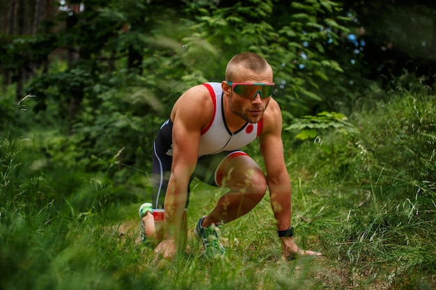 Runner homme à lunettes de soleil prêt pour un démarrage rapide dans la forêt.