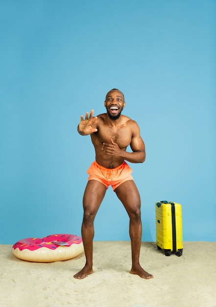 S'amuser. Heureux jeune homme au repos avec anneau de plage comme un beignet et un sac sur l'espace bleu