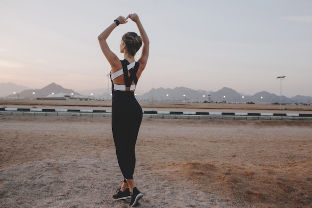 S'étendant sur la route dans un pays tropical de joyeuse belle femme au coucher du soleil. Profiter du soleil, s'entraîner en plein air, été, sportive forte, énergie, motivation, mode de vie sain.