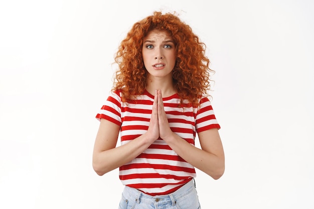 S'il vous plaît aidez-moi Sincère rousse inquiète jolie femme aux cheveux bouclés mendicité faveur presse bras ensemble plaider supplication geste fronçant les sourcils demandant des conseils prêter de l'argent debout fond blanc