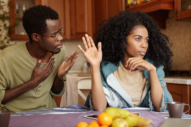 S'il vous plaît, pardonnez-moi. Malheureux tricheur afro-américain tenant la main sur sa poitrine s'excusant auprès de la belle femme indifférente qui ignorant et refusant toutes ses excuses, lui disant de se perdre