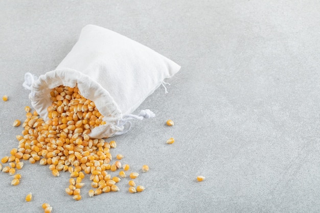 Photo gratuite un sac blanc plein de grains de maïs sur fond gris.