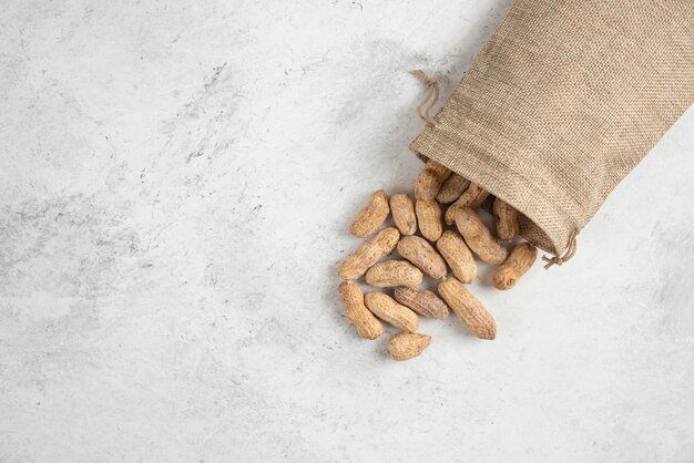 Sac de cacahuètes grillées naturelles placées sur une table en marbre.