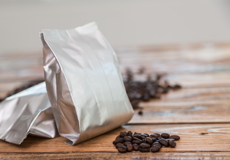 Photo gratuit sac de café métallisé avec des grains de café derrière