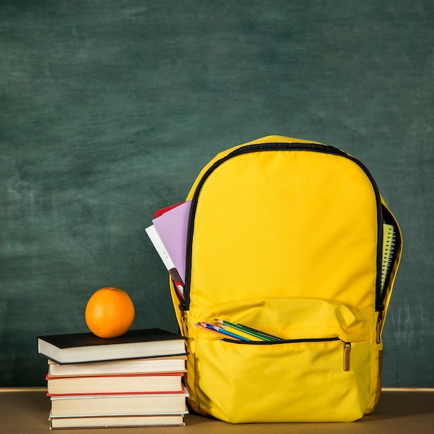 Sac à dos jaune, pile de livres et orange