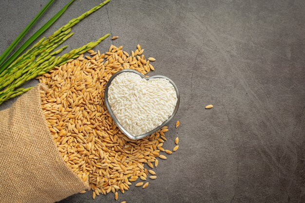 Un sac de graines de riz avec du riz blanc sur un petit bol en verre et un plant de riz