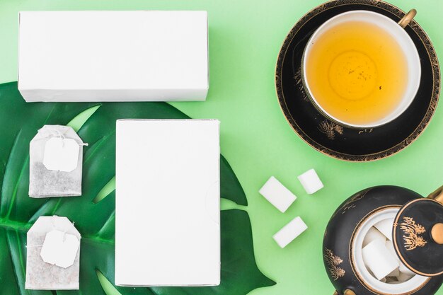 Sachets de thé, des cubes de sucre et des boîtes avec une tasse de thé à base de plantes sur fond vert