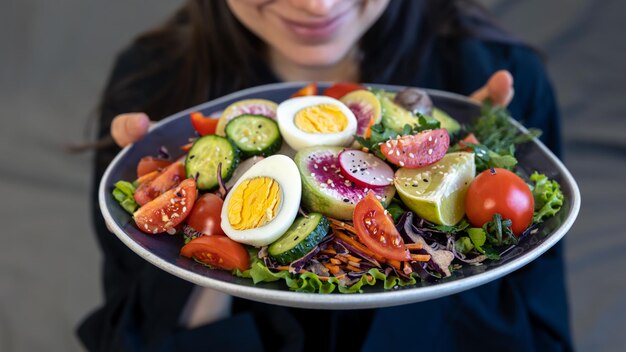 Salade appétissante avec des légumes frais et des œufs dans une assiette entre des mains féminines