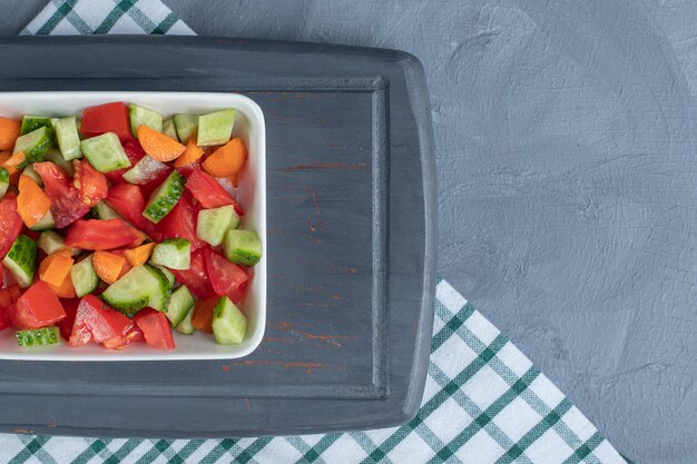 Salade de berger mélangée avec des tranches de carottes sur un plateau bleu marine sur fond de marbre.