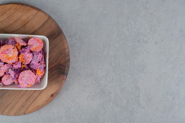 Salade de betteraves violettes avec des tranches de carottes et de la crème sure sur une planche en bois