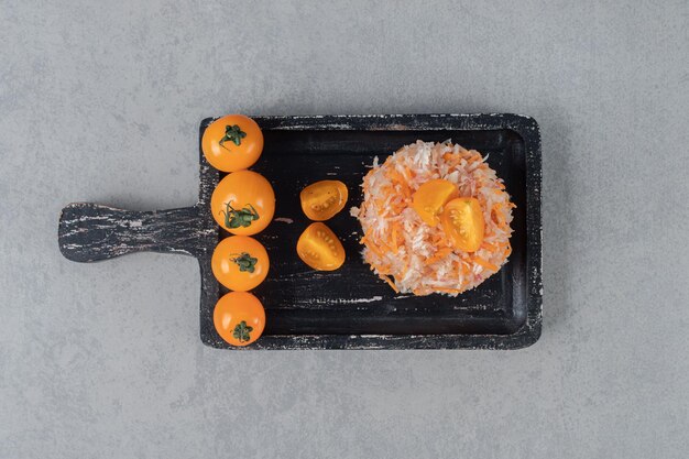 Salade de carottes aux tomates cerises jaunes sur une planche de bois.