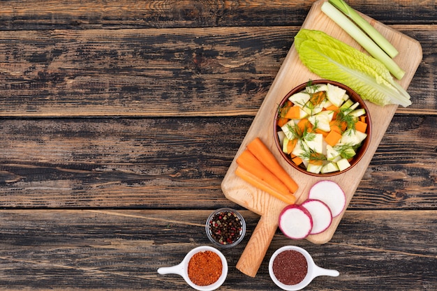 Salade de carottes dans un bol en céramique et les légumes sont sur une planche à découper en bois vue de dessus avec copie espace