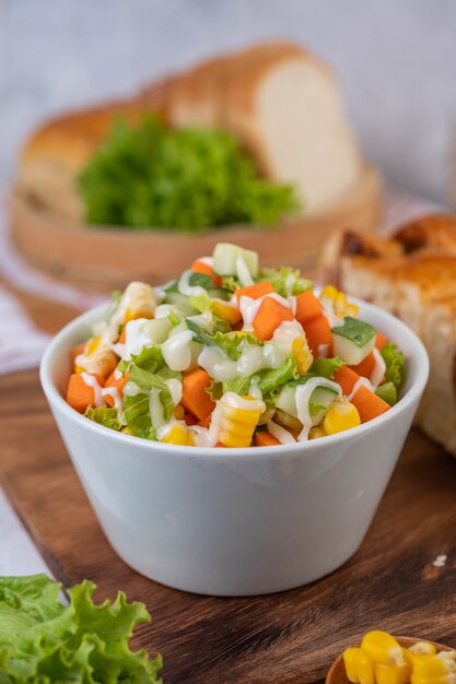 Salade de concombre, maïs, carotte et laitue dans une tasse blanche.