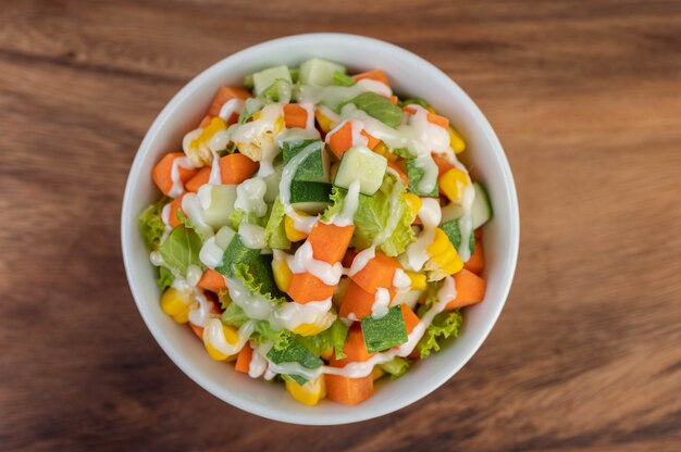 Salade de concombre, maïs, carotte et laitue dans une tasse blanche.